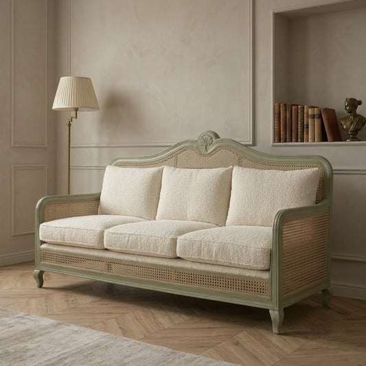 Sage green rattan cane sofa with cream boucle cushions and carved wood frame